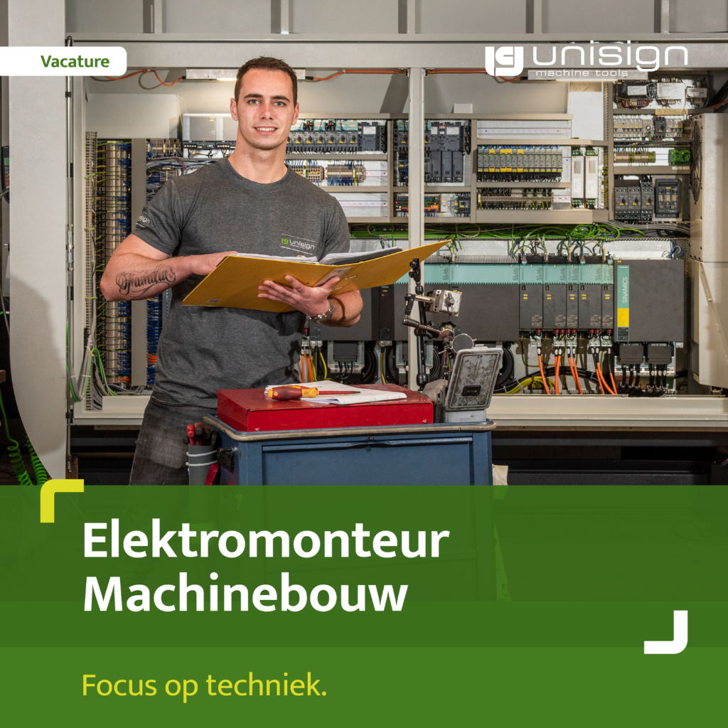 Man in a gray t-shirt stands in front of an open electrical control cabinet, holding a yellow clipboard with a recruitment banner reading 'Vacature' nearby.